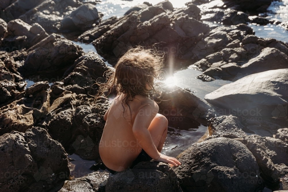 Boy sitting on rocks next to the ocean - Australian Stock Image