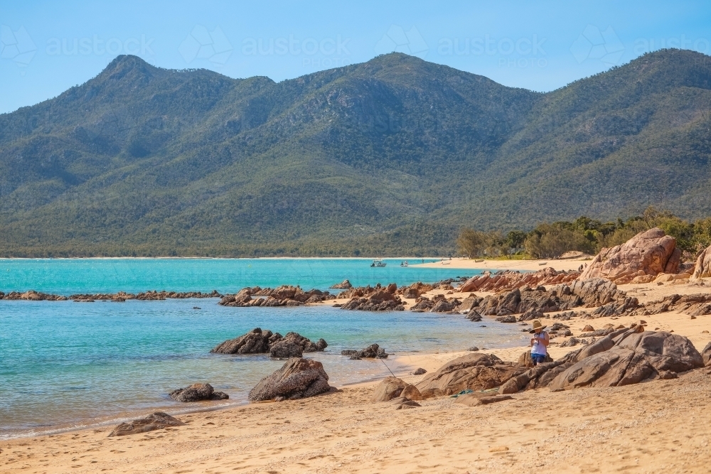 Boy standing among rocks with fishing rod at Cape Gloucester in the Whitsundays - Australian Stock Image