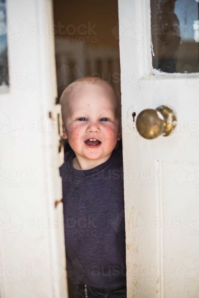 Boy standing in crack of open door smiling - Australian Stock Image