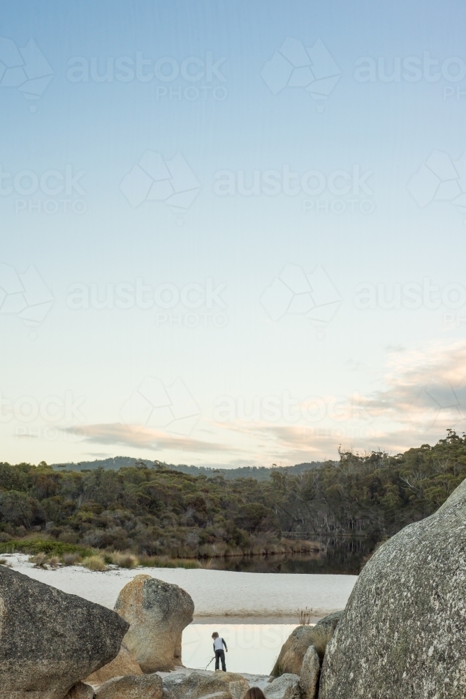 Boy surrounded by boulder rocks at beach at sunset - Australian Stock Image