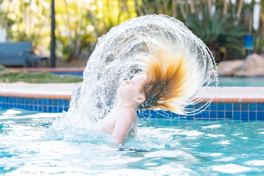 Boy swishing hair in resort swimming pool on holiday - Australian Stock Image