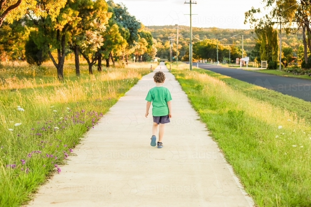 Boy walking down concrete path with green grass and trees - Australian Stock Image