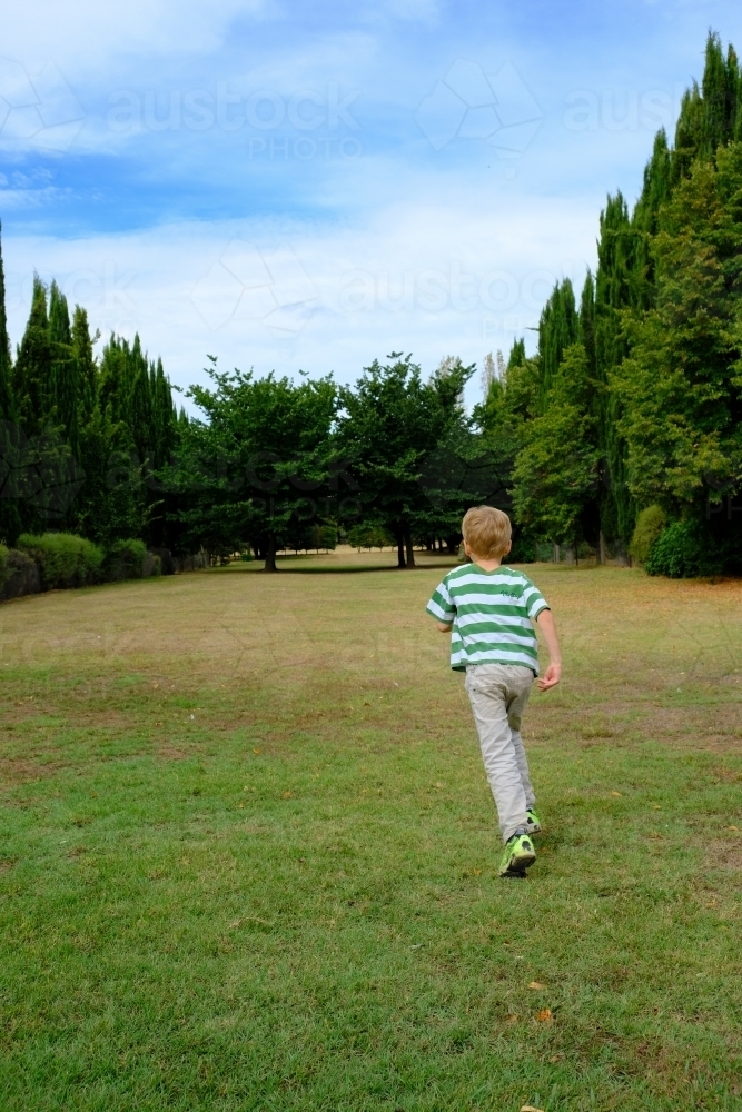 Boy walking into a large green field with trees - Australian Stock Image