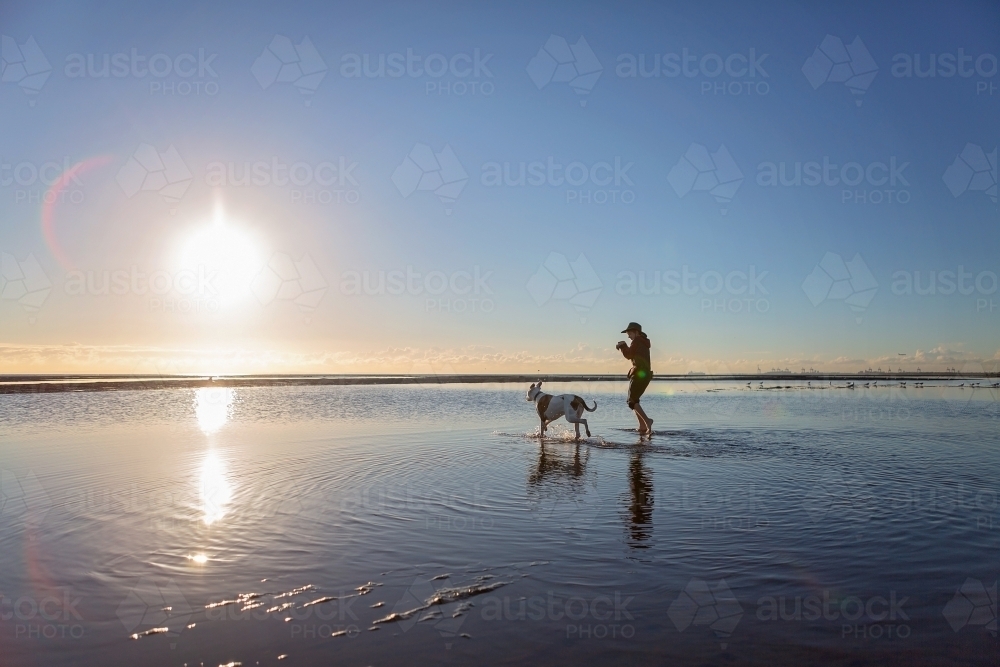 Boy walks on the beach at lowtide in winter barefoot with his dog - Australian Stock Image