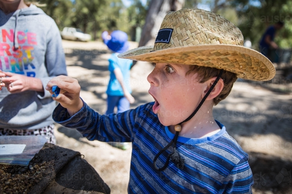 Boy wearing hat with mouth open holding tweezers with sapphire - Australian Stock Image