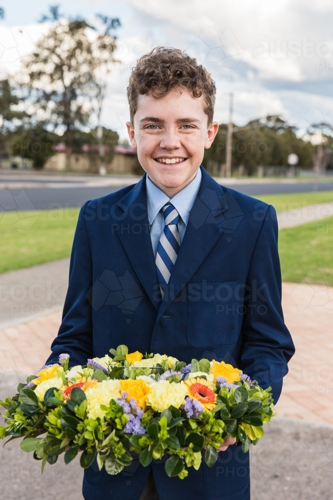 Boy wearing school uniform holding wreath for remembrance service - Australian Stock Image