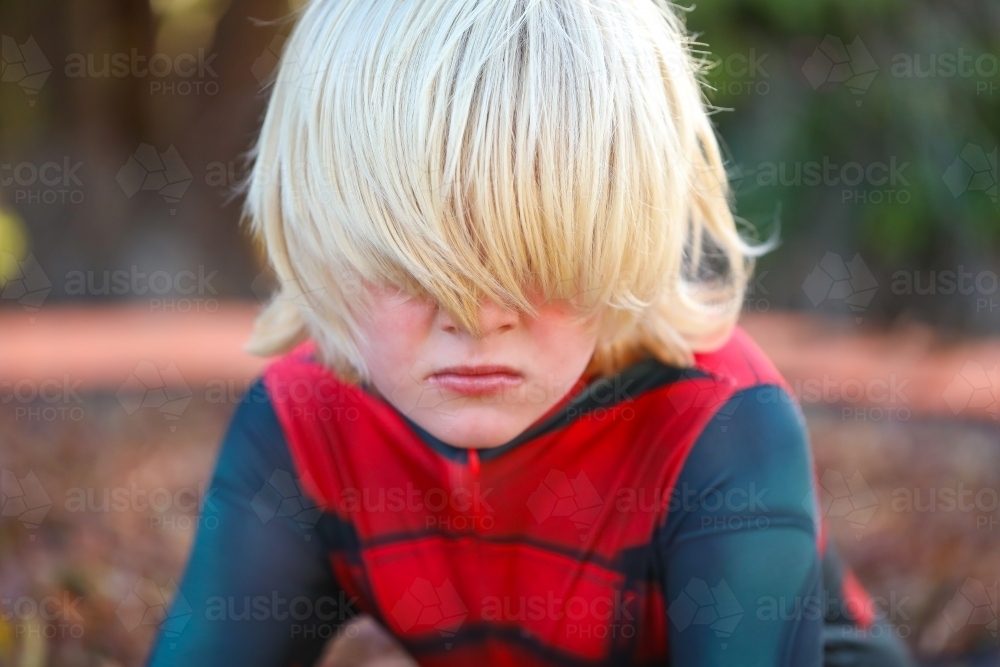 Boy wearing superhero suit with long blonde hair covering eyes - Australian Stock Image