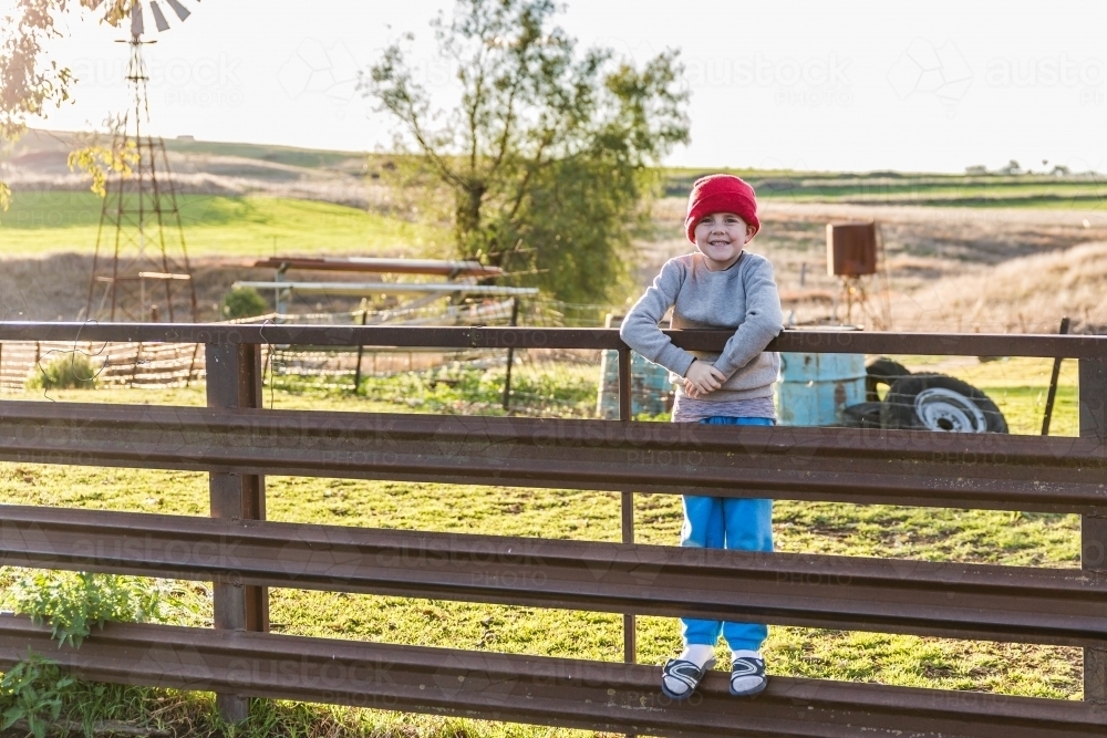 Boy with beanie standing on fence of sheep yards - Australian Stock Image