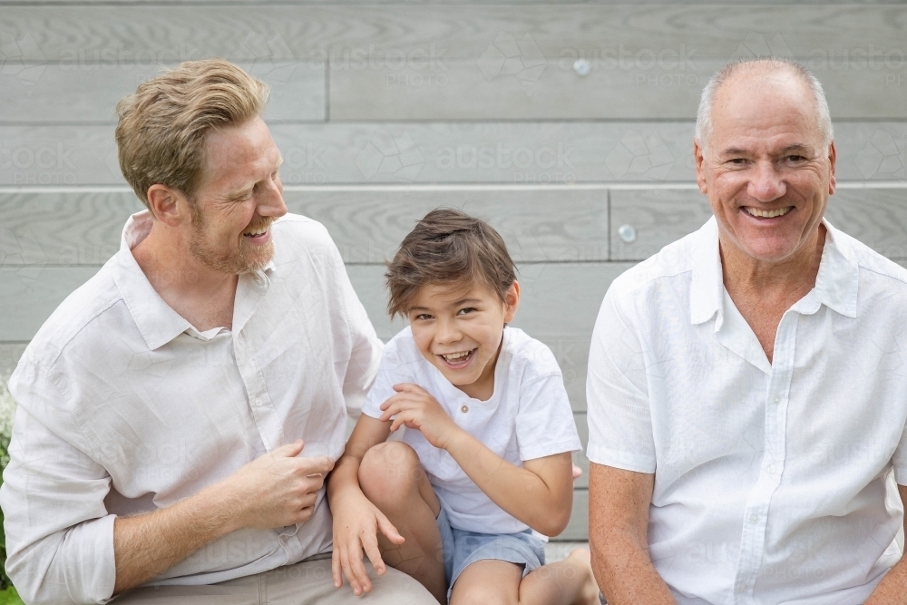 Boy with father and grandfather sitting on outdoor stairs - Australian Stock Image