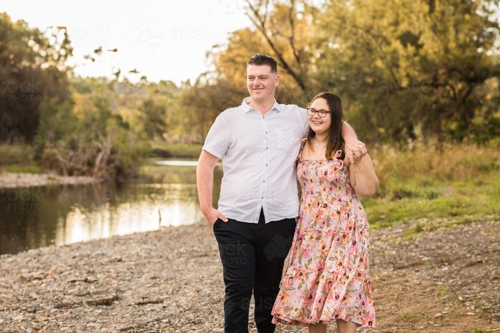 Boyfriend and girlfriend looking at water holding hands smiling - Australian Stock Image