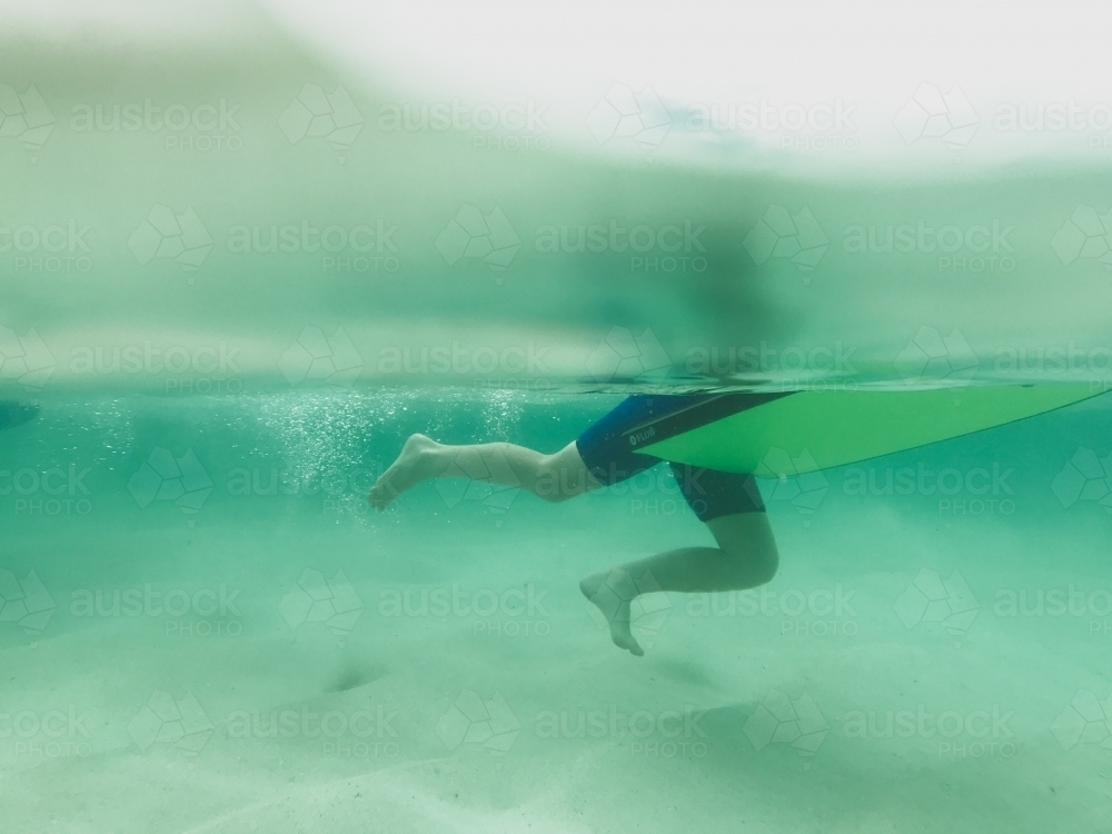 Boys legs underwater pushing off ground holding onto body board - Australian Stock Image