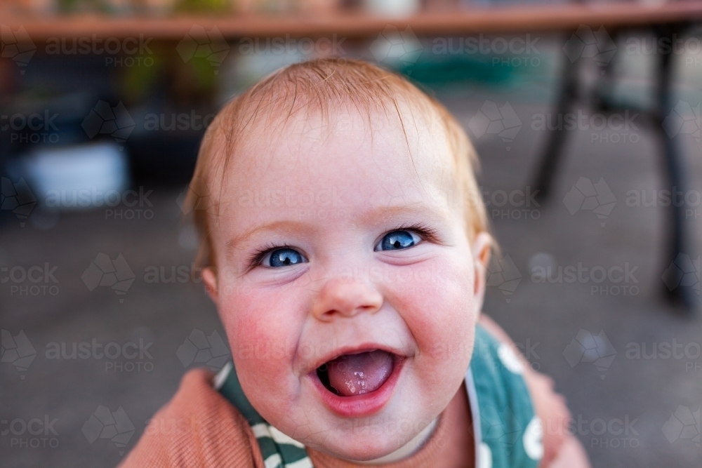 Bright blue eyes and huge smile on baby playing outdoors - Australian Stock Image