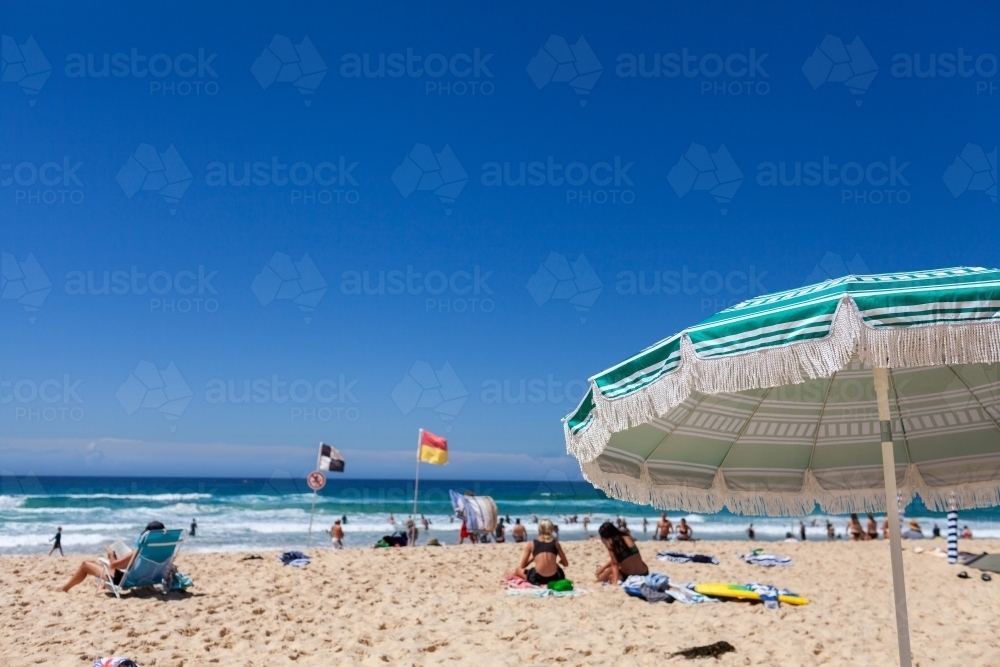 Bright summer day beach scene with bright sky and sand focus on shade umbrella - Australian Stock Image