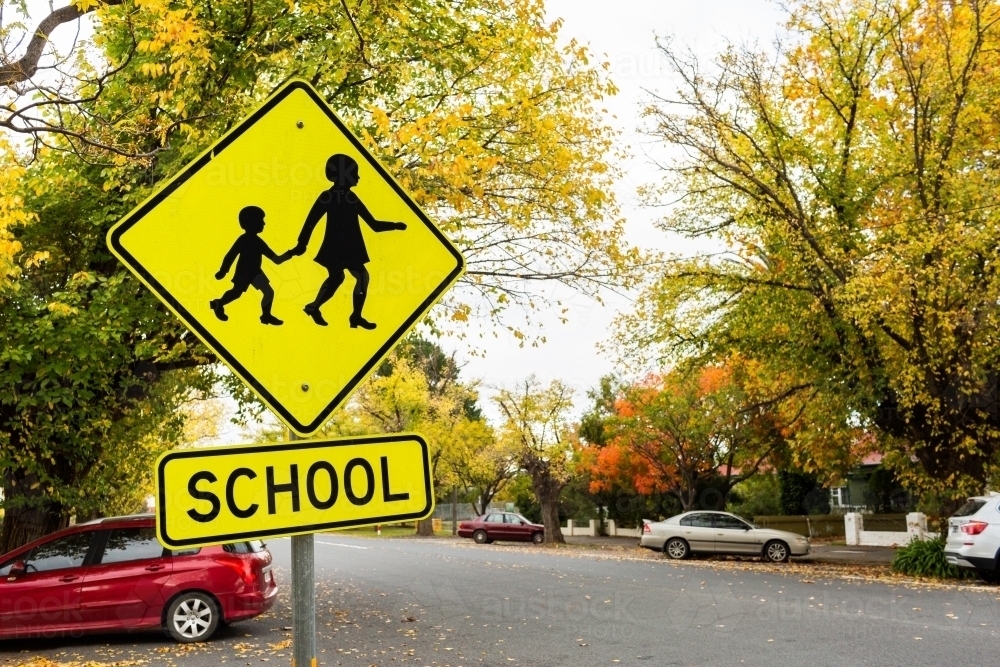 Bright yellow school sign in Autumn street with parked cars - Australian Stock Image