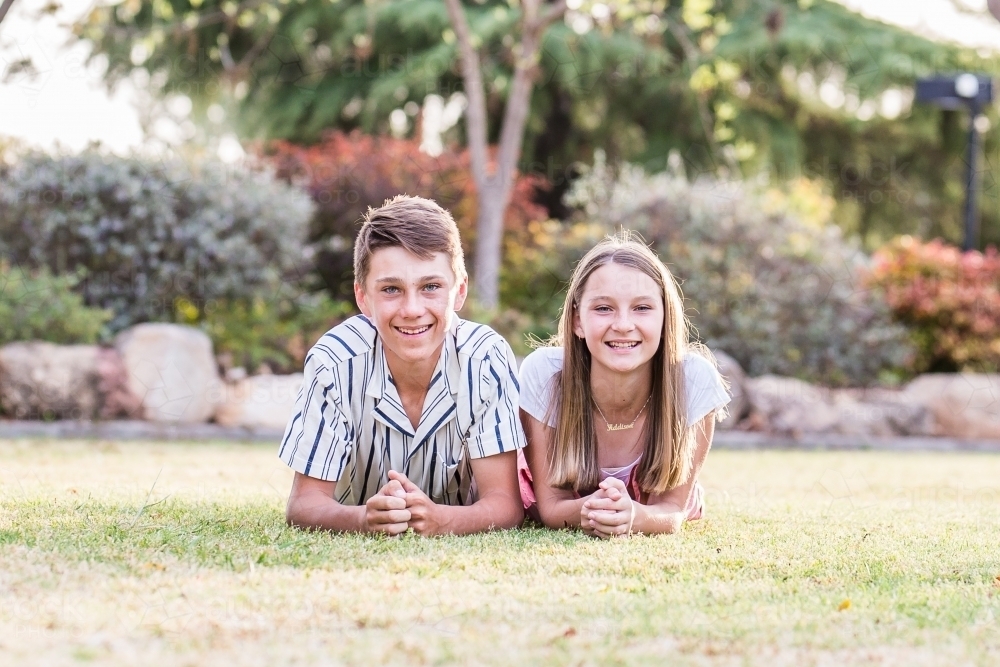 Brother and sister lying on grass smiling - Australian Stock Image