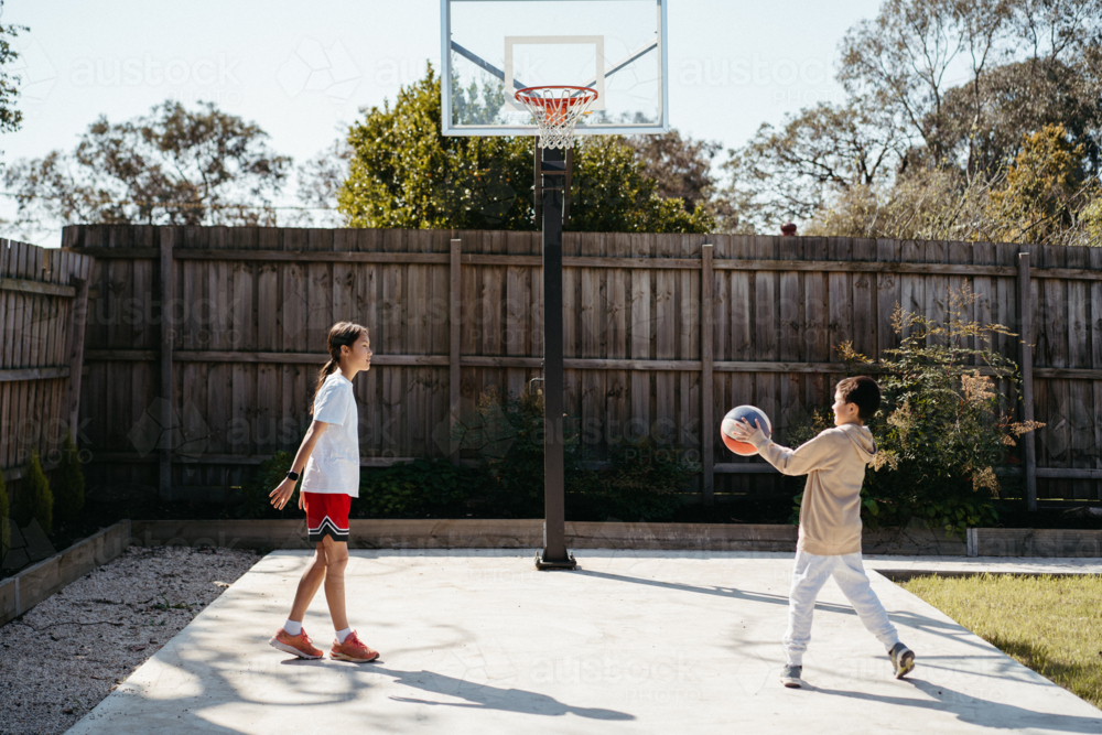 Brother and sister playing basketball in their backyard - Australian Stock Image