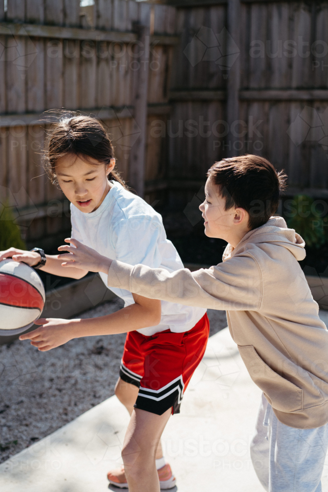 Brother and sister playing basketball in their yard. - Australian Stock Image