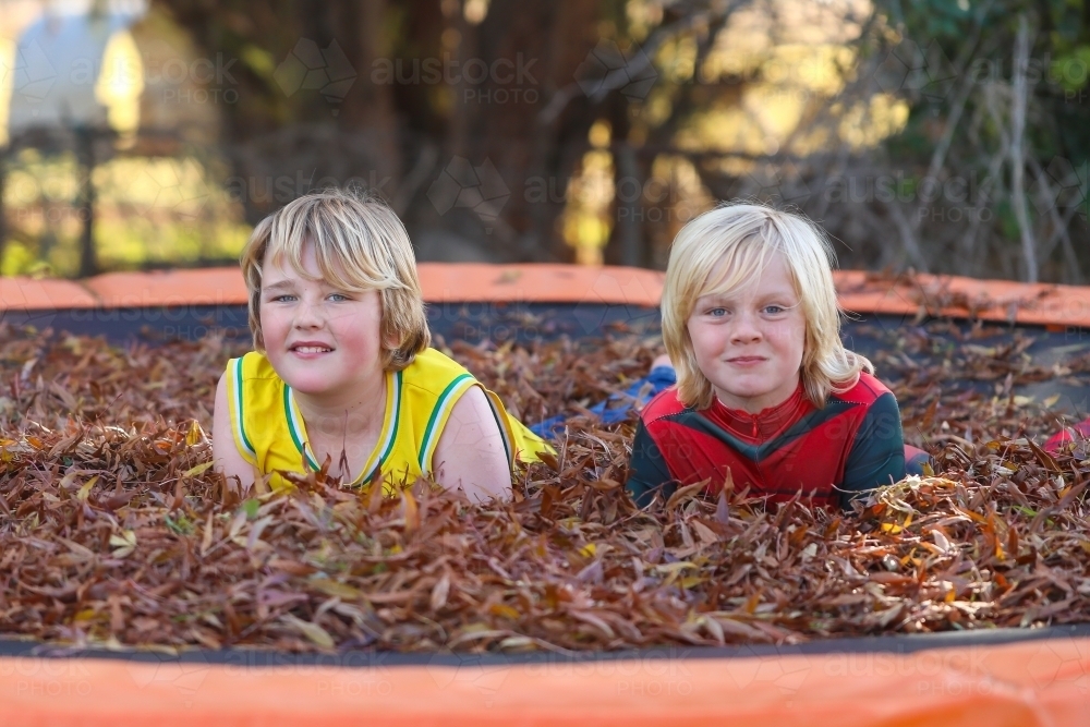 Brothers playing on trampoline covered in fallen leaves in Autumn - Australian Stock Image