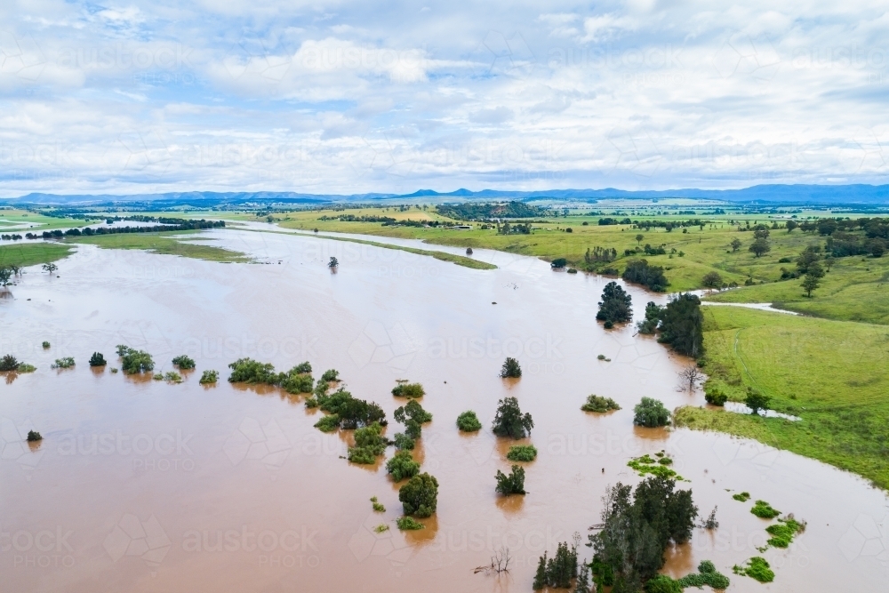 Brown floodwaters and distant farm paddocks and green hills - Australian Stock Image