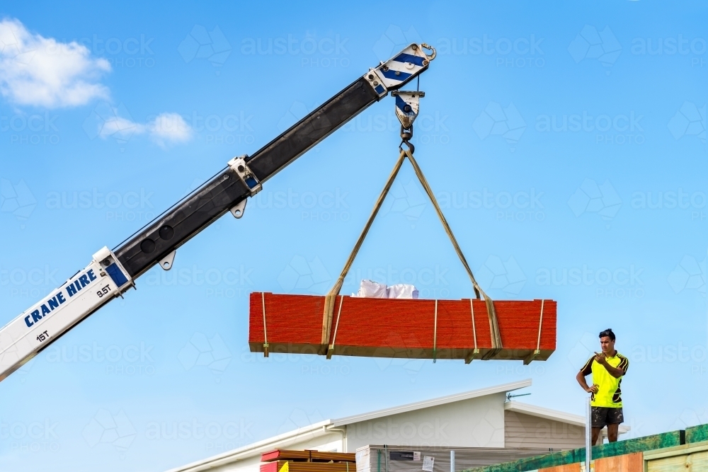 Building material being lifted by a crane to the second level with a man observing or directing - Australian Stock Image