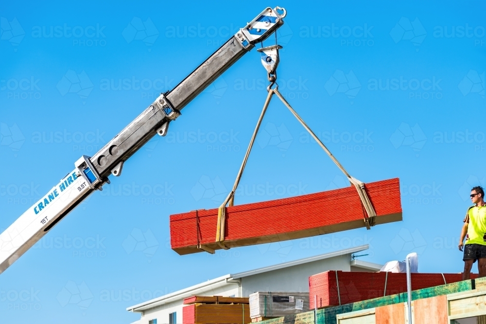 Building material being lifted by a crane to the second level with man observing - Australian Stock Image