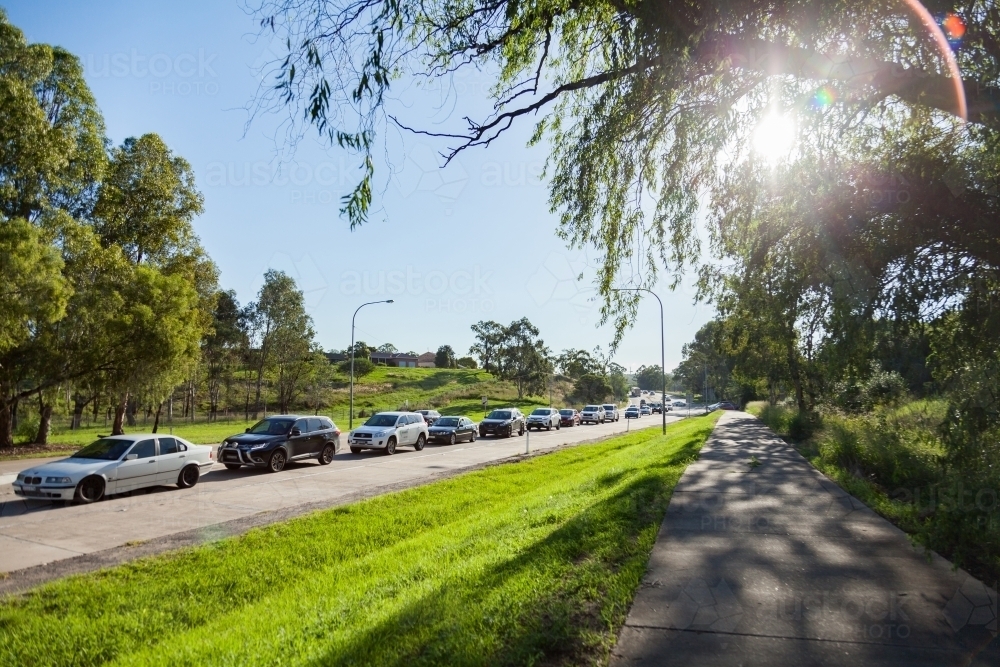 Bumper to bumper traffic on highway in singleton with footpath and sunflare - Australian Stock Image