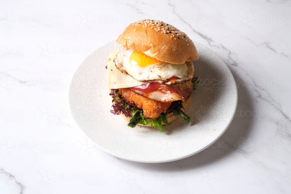 Burger on plate with egg, bacon, cheese, chicken and lettuce - Australian Stock Image