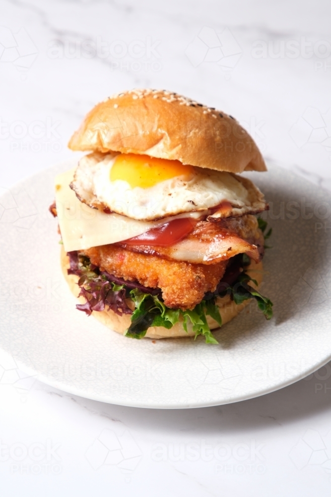 Burger on plate with egg, bacon, cheese, chicken and lettuce - Australian Stock Image