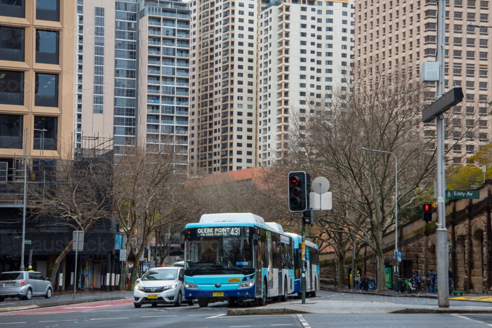 Bus at an intersection with tall buildings crowded around - Australian Stock Image