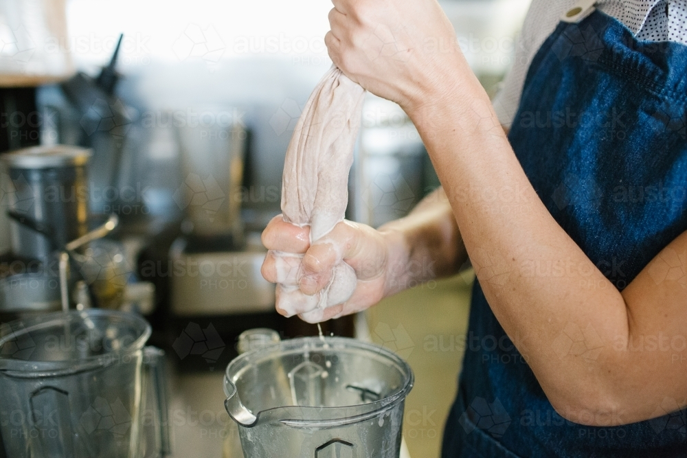 Cafe crew wearing denim apron squeezing a white cloth over container - Australian Stock Image