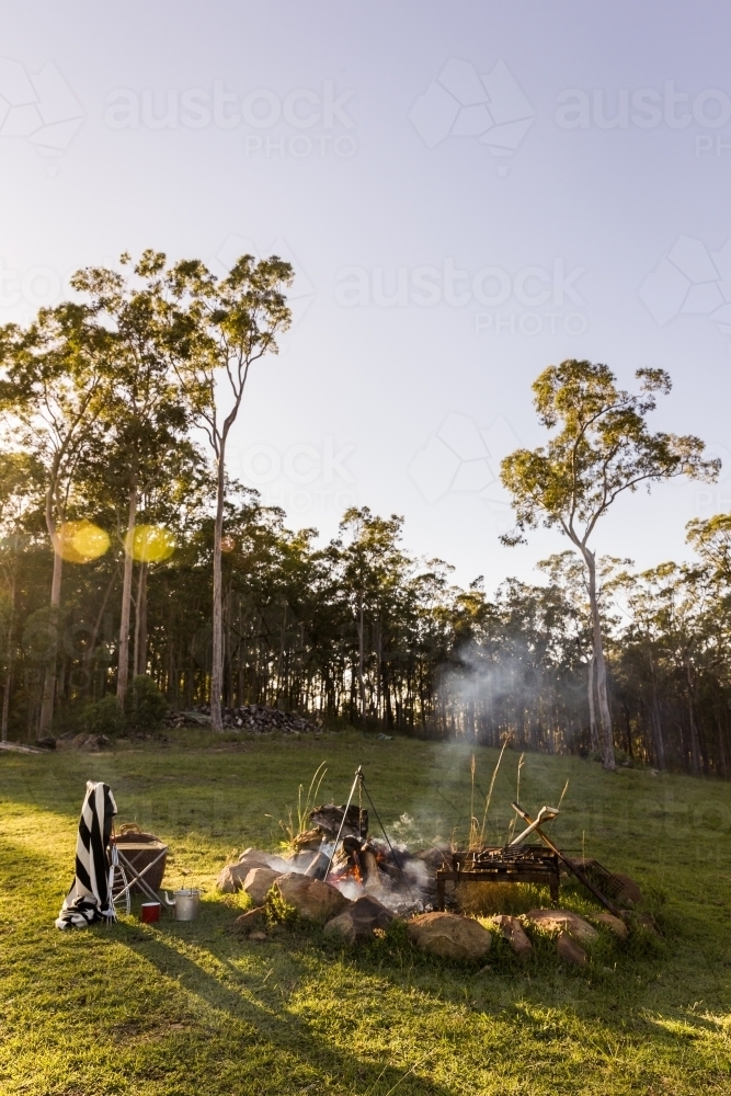 campfire and grill place with smoke and a chair with a towel in parkland - Australian Stock Image