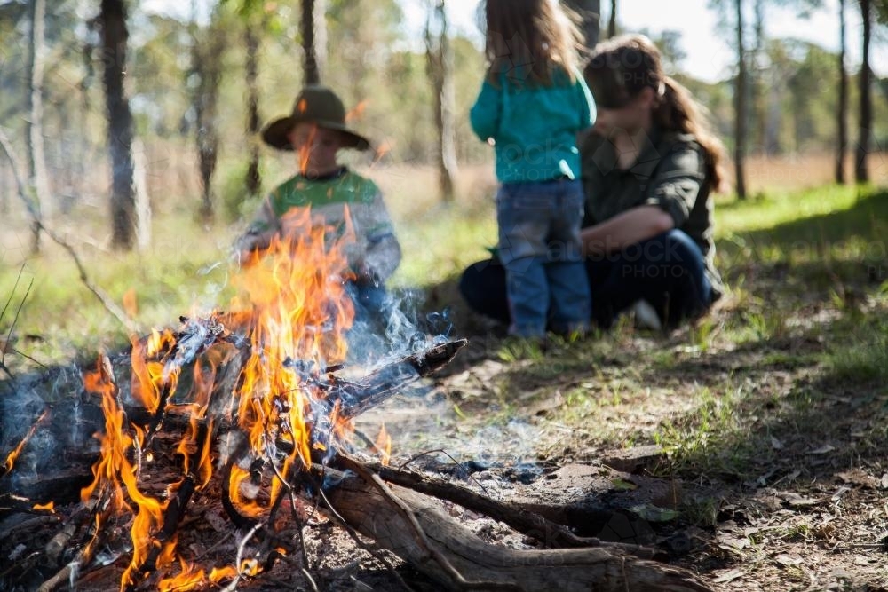 Campfire flames with out of focus people eating behind - Australian Stock Image