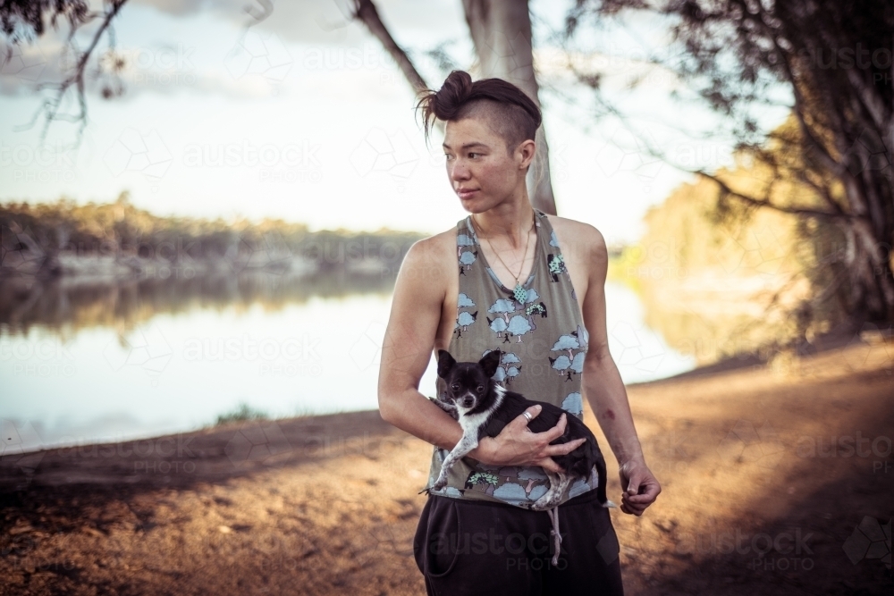 Camping life - woman holding small dog standing by a river - Australian Stock Image