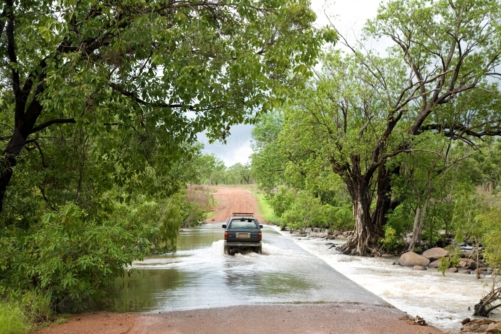 Car driving through flooding on dirt road surrounded by green trees - Australian Stock Image