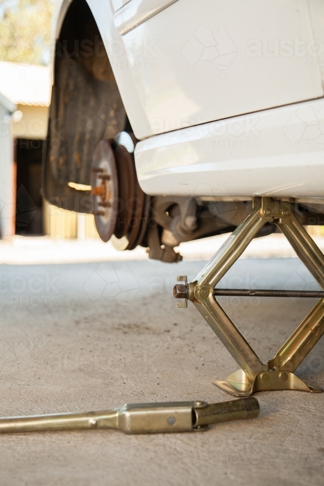 Car resting on jack while changing to spare tyre - Australian Stock Image