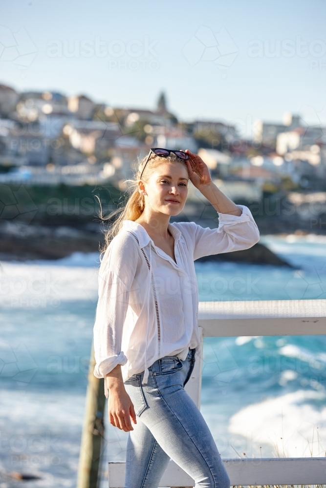 Carefree young blonde-haired woman at beach holding sunglasses - Australian Stock Image