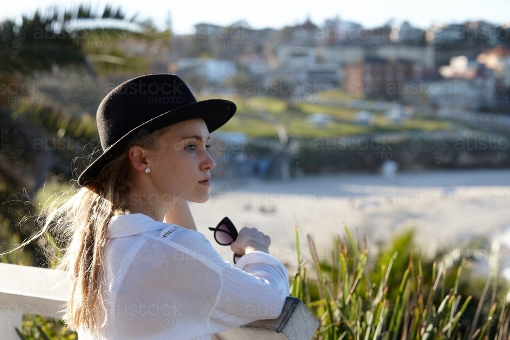 Carefree young blonde-haired woman at beach wearing black hat - Australian Stock Image