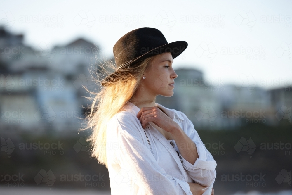 Carefree young blonde-haired woman at beach wearing black hat - Australian Stock Image