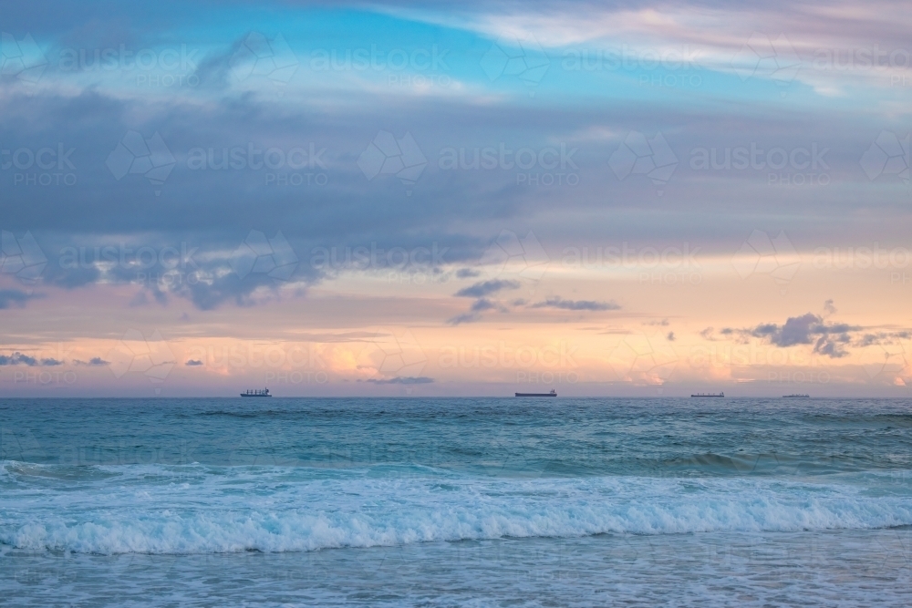 Cargo ships lined up at sea en route to Newcastle Harbour under a vibrant sunset sky - Australian Stock Image