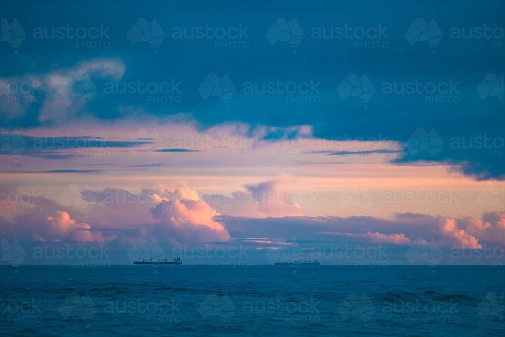 Cargo ships lined up at sea on their way to Newcastle Harbour under a vibrant sunset sky - Australian Stock Image