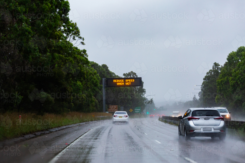 Cars traveling on slippery road with digital sign warning of hazardous driving conditions - Australian Stock Image