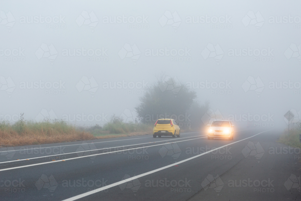 Cars travelling on highway road through fog with low visibility - Australian Stock Image