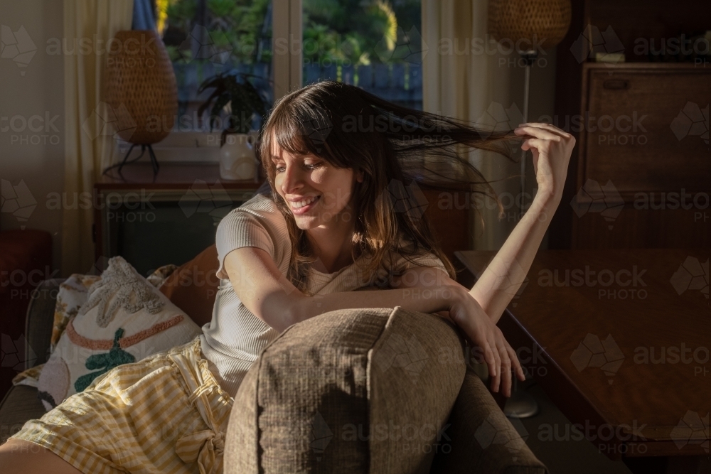 casual woman sitting on her sofa in the afternoon sunlight - Australian Stock Image