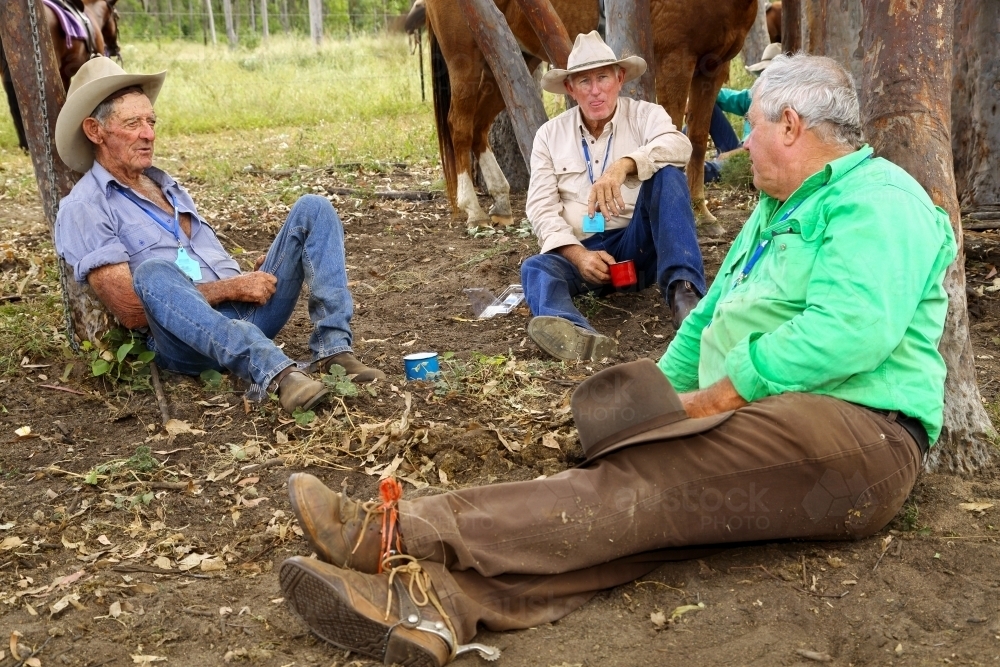 Cattle drovers sitting resting against trees at smoko. - Australian Stock Image