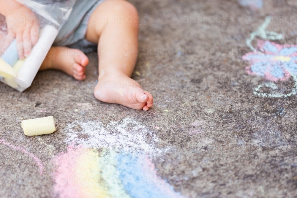 chalk covered foot of baby on concrete with rainbow art drawing - Australian Stock Image