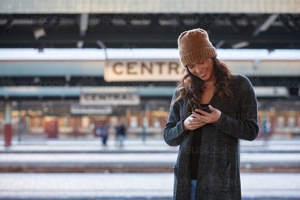 Cheerful Asian woman waiting at train station with mobile phone - Australian Stock Image