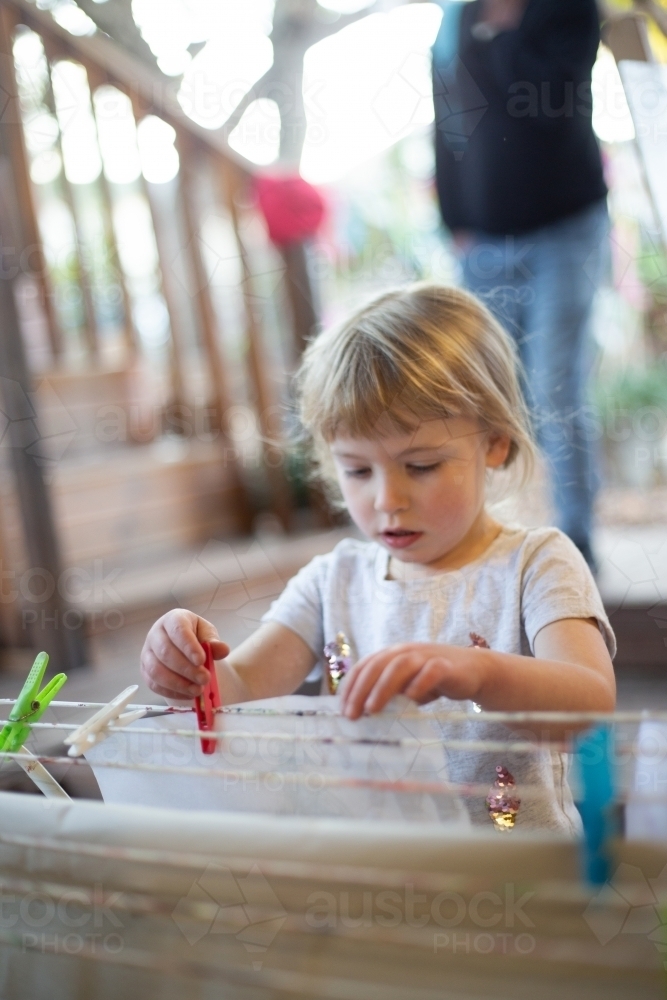 Child carefully pegs a picture at preschool to dry - Australian Stock Image