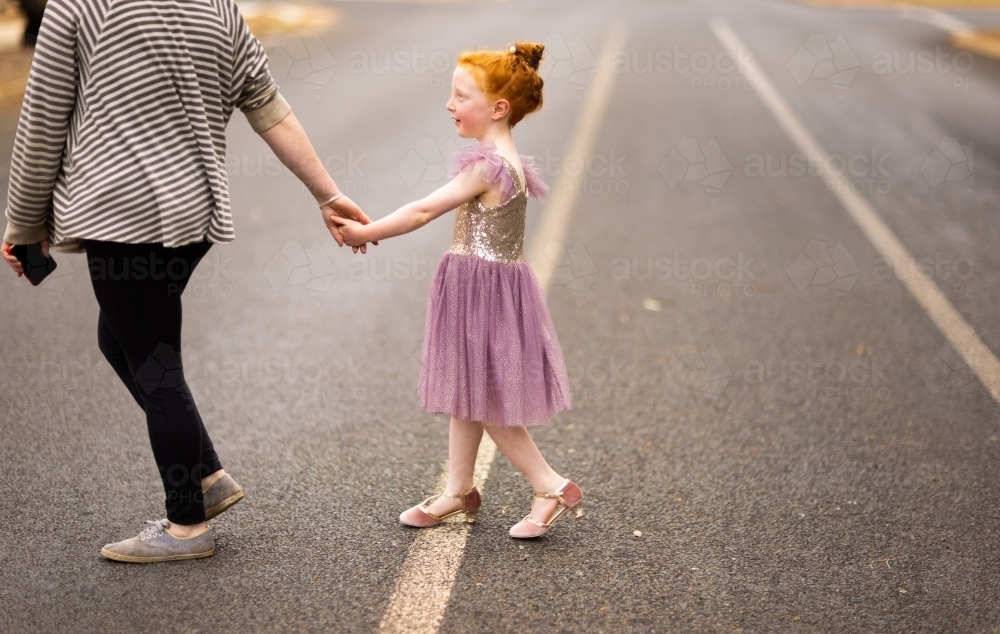 child holding adult's hand while crossing street safely - Australian Stock Image