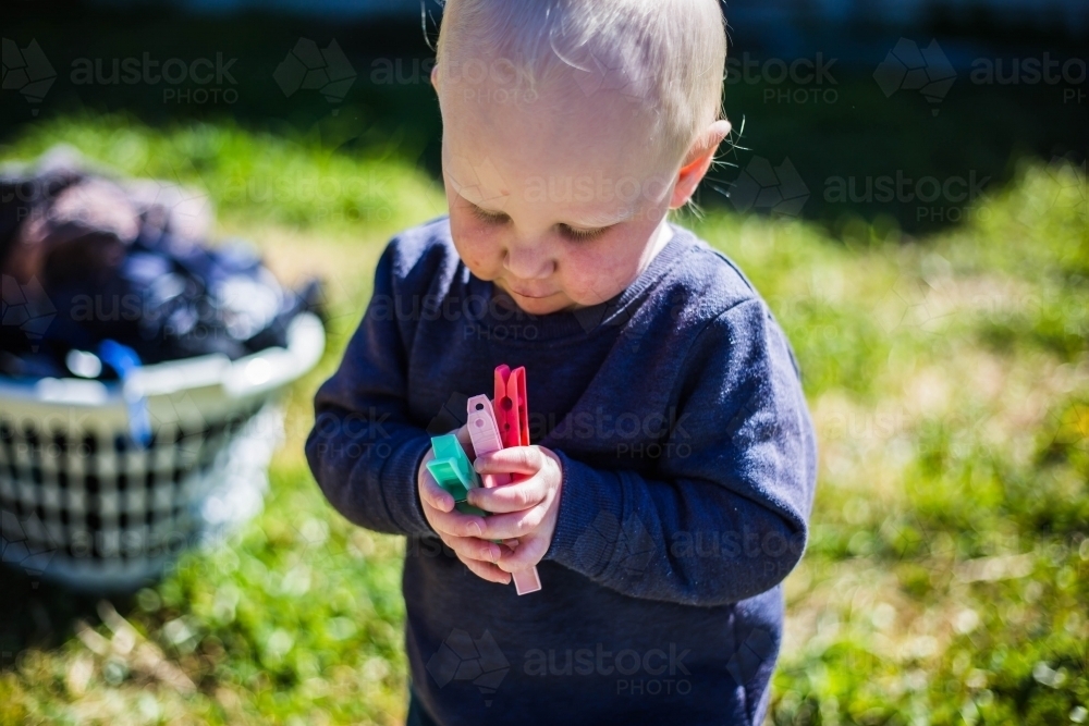 Child holding pegs with green grass and basket of washing - Australian Stock Image