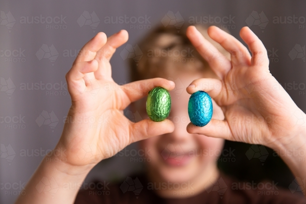 child holding up Easter eggs between fingers - Australian Stock Image